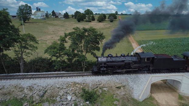 Aerial View of An Antique Restored Steam Locomotive Blowing Smoke and Steam Traveling Thru Farmlands and Countryside on a Sunny Summer Day