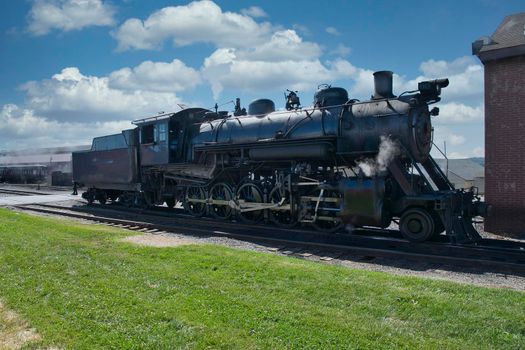 View of An Antique Restored Steam Locomotive Blowing Smoke and Steam Traveling Thru Farmlands and Countryside on a Sunny Summer Day