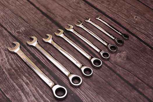 Set of combination wrenches on a wooden background. top view. eight brilliant ones steel open-end keys for repair with a ratchet
