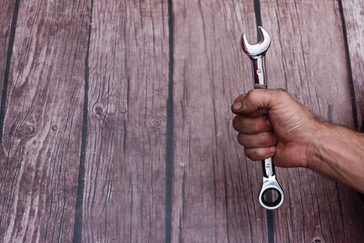 A combination wrench in a rough, smeared man's hand. On a wooden background, close-up.