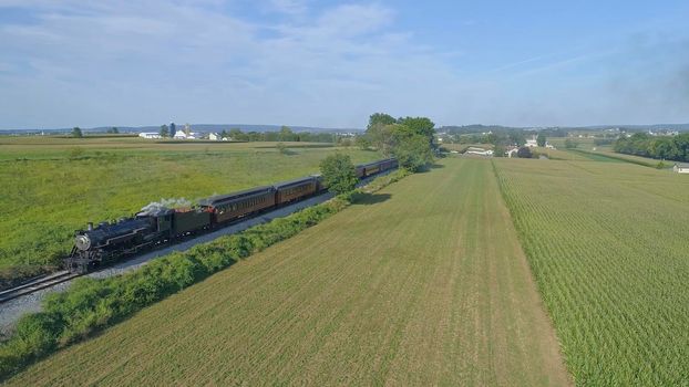 Aerial View of An Antique Restored Steam Locomotive Blowing Smoke and Steam Traveling Thru Farmlands and Countryside on a Sunny Summer Day