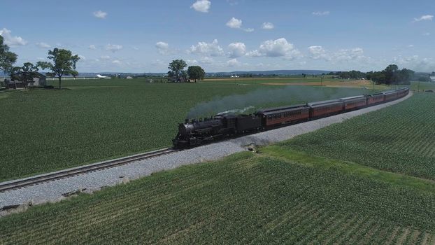 Aerial View of An Antique Restored Steam Locomotive Blowing Smoke and Steam Traveling Thru Farmlands and Countryside on a Sunny Summer Day