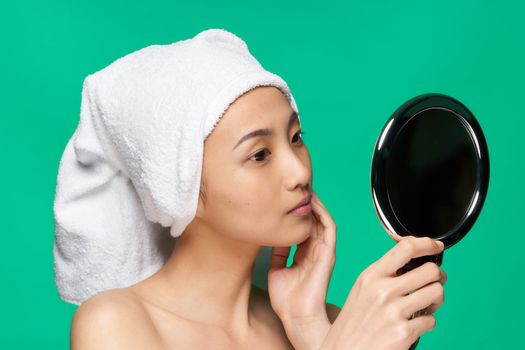 woman of asian appearance looks in the mirror with a towel on her head clean skin. High quality photo
