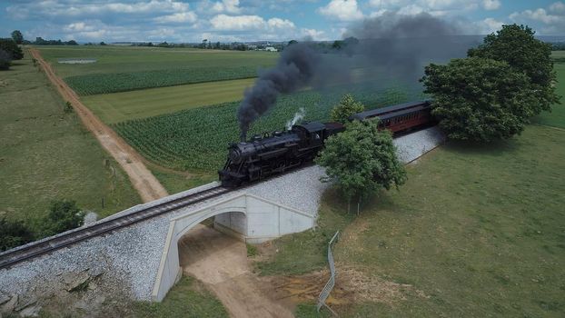 Aerial View of An Antique Restored Steam Locomotive Blowing Smoke and Steam Traveling Thru Farmlands and Countryside on a Sunny Summer Day