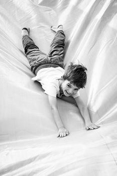 Smiling little boy playing on inflatable slide, looking at camera, black and white shot