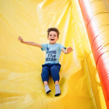 Smiling little boy playing on inflatable slide, looking at camera