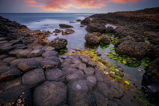 sunset over basalt rocks formation Giant's Causeway, Port Ganny Bay and Great Stookan, County Antrim, Northern Ireland, UK