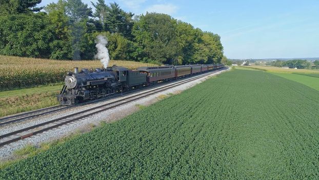 Aerial View of An Antique Restored Steam Locomotive Blowing Smoke and Steam Traveling Thru Farmlands and Countryside on a Sunny Summer Day