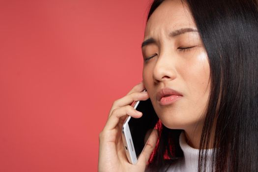 brunette asian appearance talking on the phone technology studio red background. High quality photo