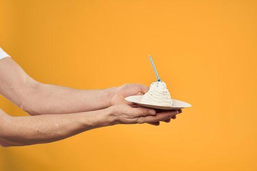 Cake with a candle in a man's hand on a yellow background cropped view Copy Space. High quality photo