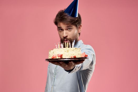 Man with cake in a plate and in a blue shirt on a pink background birthday holidays cropped view. High quality photo