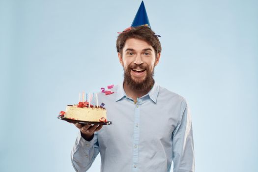 Man with a plate of cake and a festive candle blue background cap corporate party. High quality photo