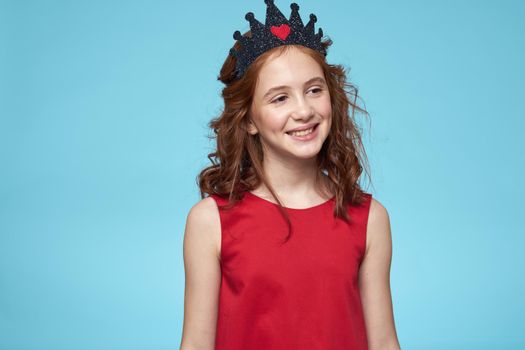 Girl with curly hair with a crown on her head red dress lifestyle blue background. High quality photo