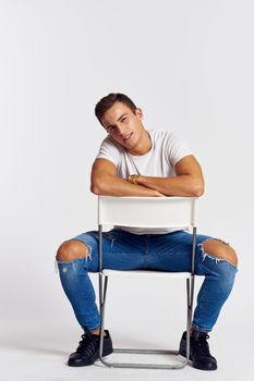 A man in jeans sits on a chair backwards and and ripped jeans T-shirt front view. High quality photo