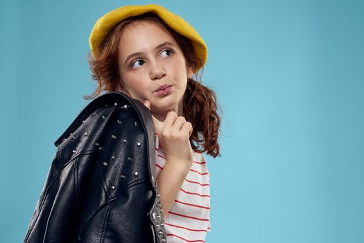 Fashionable girl in a yellow beret and leather jacket striped T-shirt blue background. High quality photo