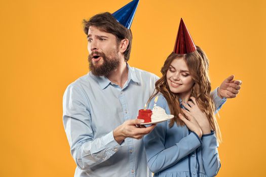 Birthday party man and woman in a cap with a cake on a yellow background cropped view. High quality photo