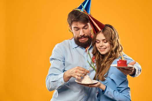 Man and woman at a party in caps and with tinsel cake fun yellow background. High quality photo