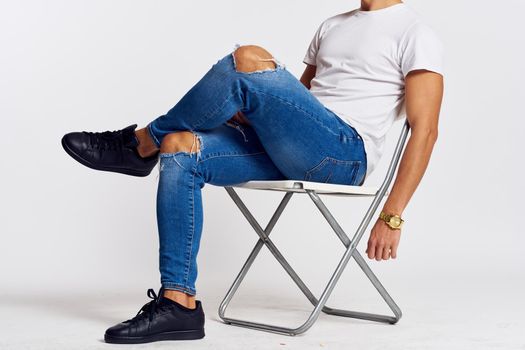a man in jeans and a t-shirt sits on a chair on a light background side view. High quality photo