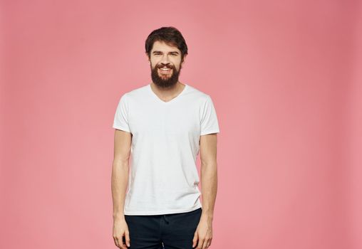 Bearded guy in a T-shirt and trousers on a pink background. High quality photo