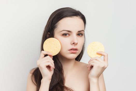 pretty brunette naked shoulders wipes her face but clean skin with a sponge. High quality photo