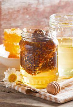 Close up honeycomb with honey in glass jar on wooden board, top view