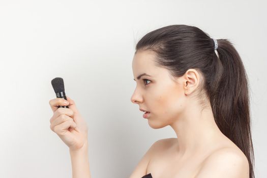 woman with bare shoulders applying makeup brush on face procedure. High quality photo