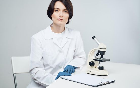 woman doctor in a medical gown with a microscope on the table sits on a chair in a bright room. High quality photo