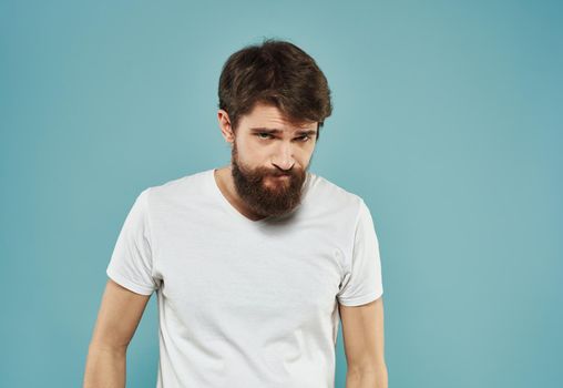 A man in a white T-shirt and with a thick beard on a blue background gestures with his hands. High quality photo