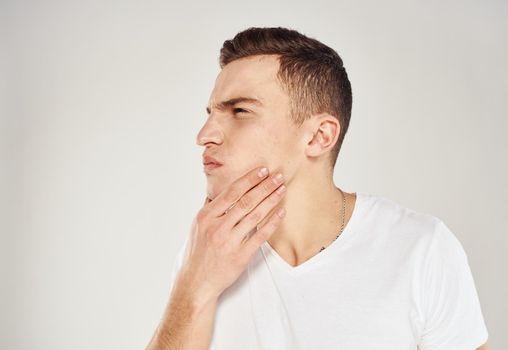 A man on a light background touches his face with his hand and a white T-shirt model. High quality photo