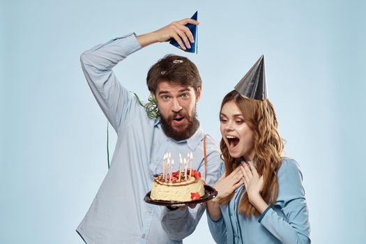 Cheerful man and woman blowing out cake candles holiday decoration blue background. High quality photo