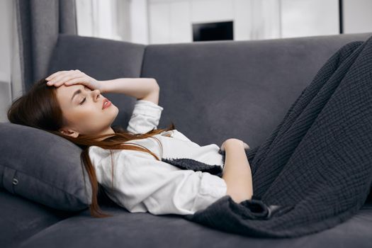 woman covered with a blanket lies on the sofa hand on her head feeling unwell. High quality photo