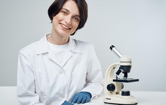 woman doctor in a medical gown with a microscope on the table sits on a chair in a bright room. High quality photo