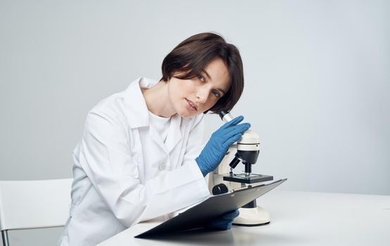 woman doctor in a medical gown with a microscope on the table sits on a chair. High quality photo