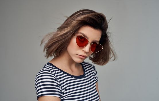 beautiful woman with glasses and striped t-shirt red skirt gray background. High quality photo