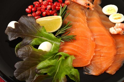 A seafood dish. Sliced salmon slices on a beautiful black plate with lemon, shrimp, quail egg and herbs and a red background. High quality photo