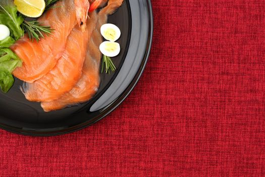 Salmon. Slices of red salted fish on a black plate, a beautiful seafood dish decorated with lemon pomegranate greens and quail egg. Fled lei. High quality photo