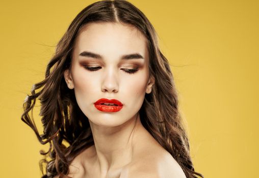 Portrait of a beautiful lady with red lips brunette eyeshadow on the eyelids yellow background. High quality photo