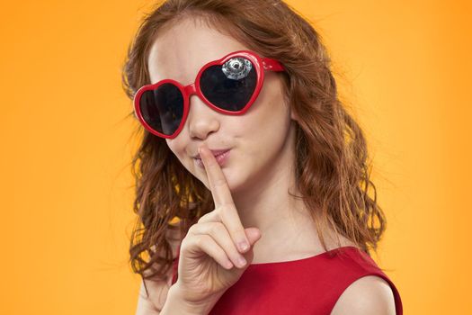 Cheerful cute girl glasses in the form of a heart fashion close-up yellow background. High quality photo