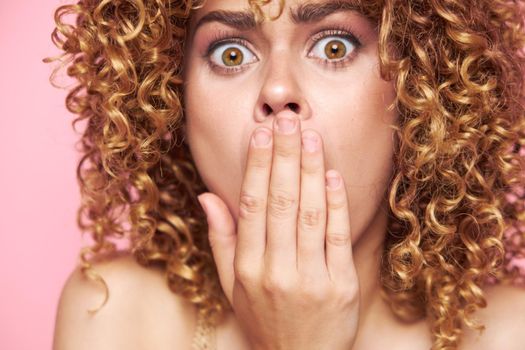 Beautiful woman looking at the camera in surprise and covering her mouth with her hands bright makeup pink isolated background