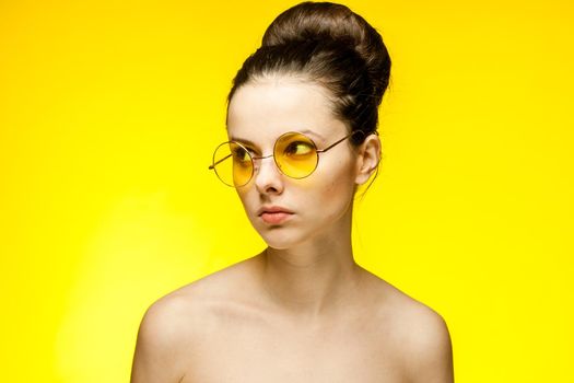 woman with bare shoulders yellow glasses hands near face clear skin. High quality photo