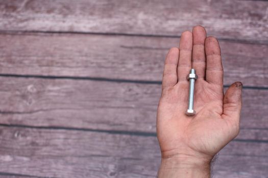 Bolt and nut. In the man's hand, smeared with work, lies a screw with a screwed nut. On a wooden background. copy space