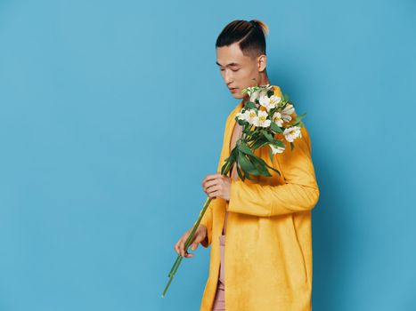 Fashionable man in a yellow coat holding a bouquet of white flowers, Asian appearance model. High quality photo