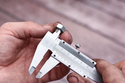 Measuring the diameter of the nut thread with a caliper. The worker's hands are dirty from work.