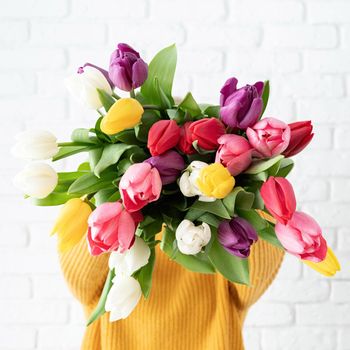 Mothers Day, Women's Day concept. Spring holidays. Woman in yellow holding bouquet of tulips in front of her face