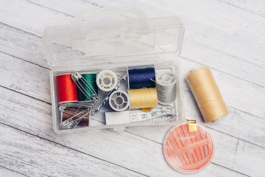 thread needles sewing supplies in a plastic box on a wooden background. High quality photo