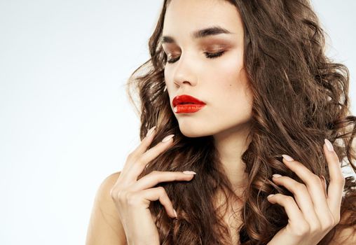Beautiful brunette woman with bright makeup touches curly hair on her head with her hands. High quality photo