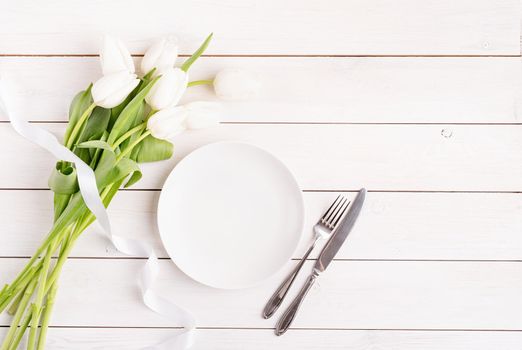 Concept Spring, Easter or Mother's Day. Festive table setting in white, white plate and tulips top view on wooden background