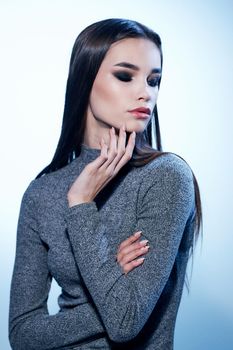 Beautiful woman in a gray sweater gestures with her hands and makeup with eyeshadow on her eyelids. High quality photo