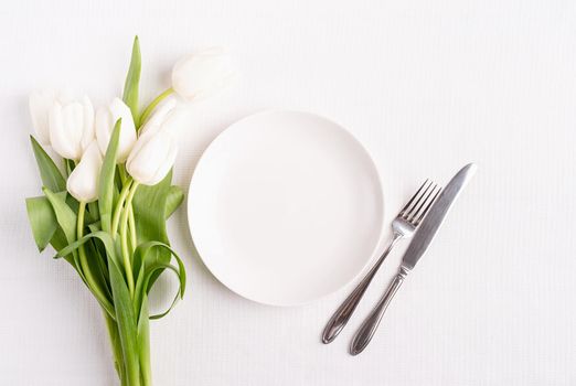 Concept Spring, Easter or Mother's Day. Festive table setting in white, white plate and tulips top view on background