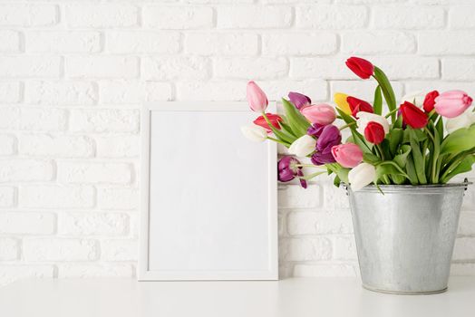 Bucket of fresh tulip flowers and blank frame over white brick wall background. Mock up design